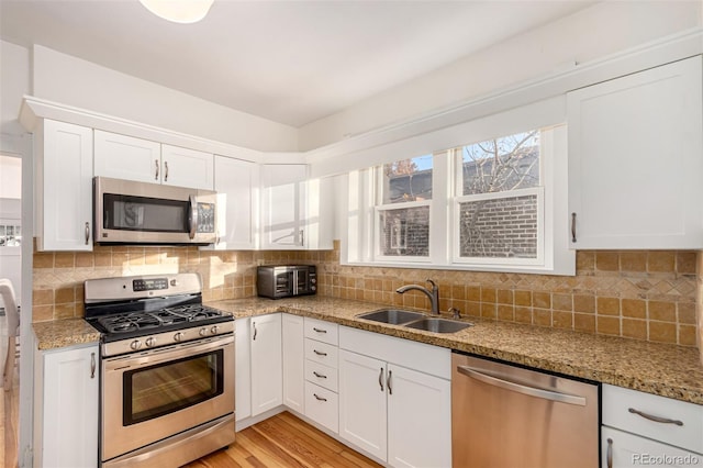 kitchen with light stone countertops, stainless steel appliances, sink, white cabinets, and light hardwood / wood-style floors