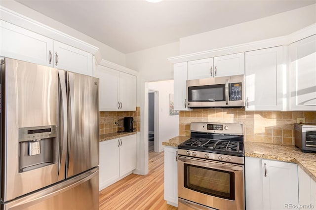 kitchen with white cabinets, light stone counters, light wood-type flooring, and appliances with stainless steel finishes