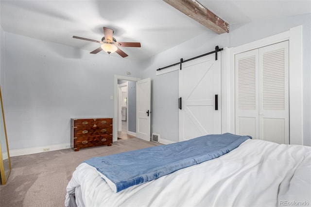 bedroom with ceiling fan, a barn door, beamed ceiling, light colored carpet, and a closet