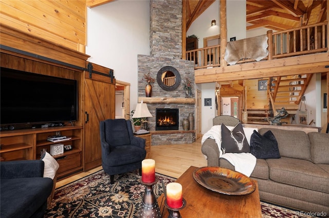 living room featuring a stone fireplace, beam ceiling, wood-type flooring, a barn door, and high vaulted ceiling