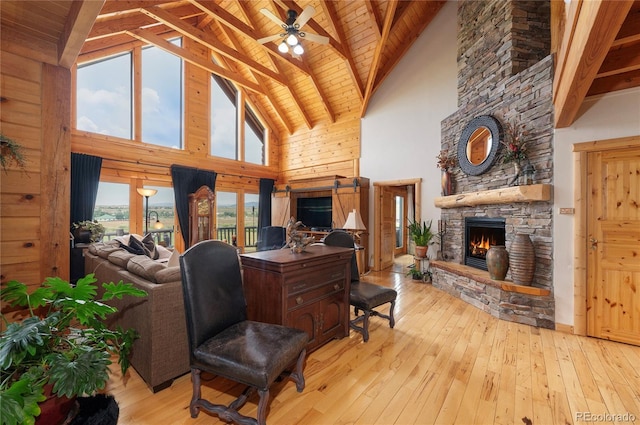 living room featuring wood ceiling, a stone fireplace, light hardwood / wood-style floors, beam ceiling, and high vaulted ceiling