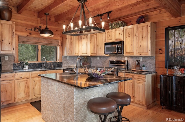 kitchen featuring pendant lighting, appliances with stainless steel finishes, a kitchen island with sink, and wood walls