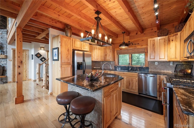 kitchen featuring a kitchen island with sink, stainless steel appliances, hanging light fixtures, and light wood-type flooring