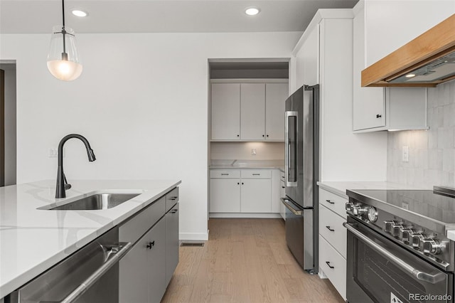 kitchen with premium appliances, white cabinets, hanging light fixtures, sink, and light wood-type flooring