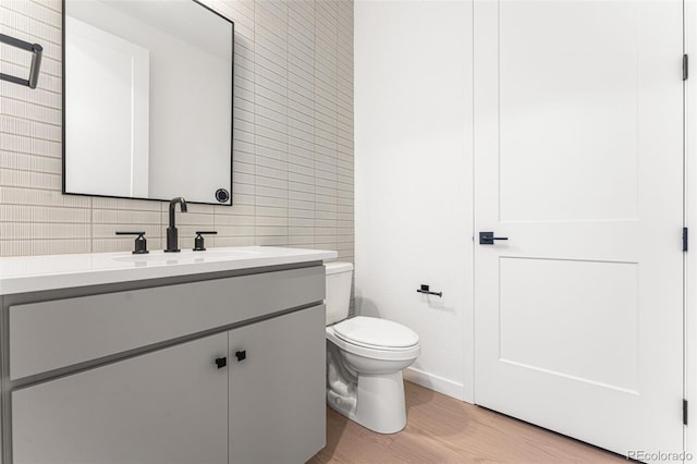 bathroom featuring wood-type flooring, toilet, tile walls, tasteful backsplash, and vanity