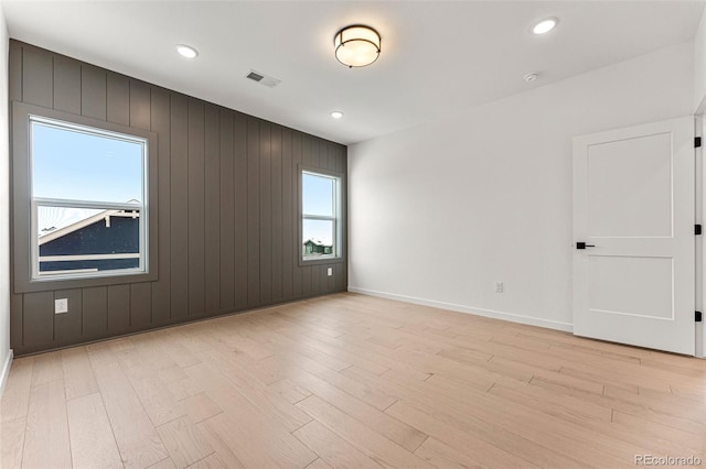 unfurnished room with light hardwood / wood-style floors and wooden walls