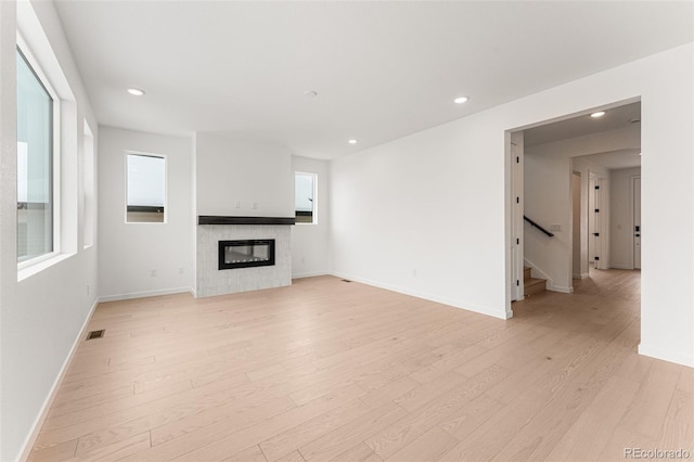 unfurnished living room with a tiled fireplace and light hardwood / wood-style flooring