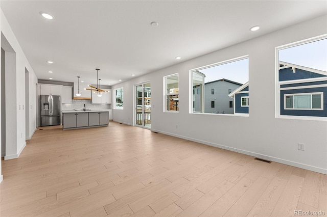 unfurnished living room featuring a chandelier, sink, and light hardwood / wood-style flooring