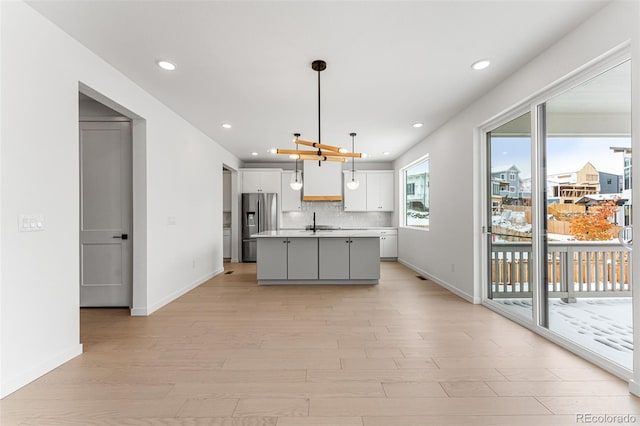 kitchen featuring light hardwood / wood-style floors, a center island with sink, white cabinetry, stainless steel fridge with ice dispenser, and pendant lighting