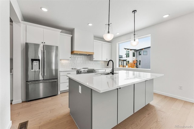 kitchen featuring white cabinetry, stainless steel appliances, a center island with sink, and decorative light fixtures