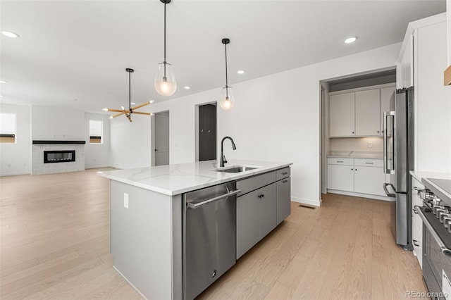 kitchen with a kitchen island with sink, appliances with stainless steel finishes, decorative light fixtures, sink, and light hardwood / wood-style flooring