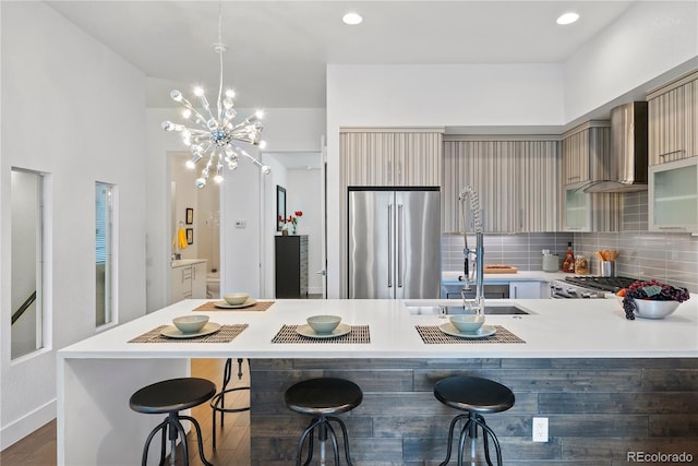 kitchen with a kitchen bar, stainless steel fridge, stove, wall chimney exhaust hood, and sink