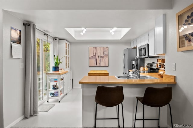 kitchen featuring stainless steel appliances, white cabinetry, sink, a kitchen breakfast bar, and kitchen peninsula