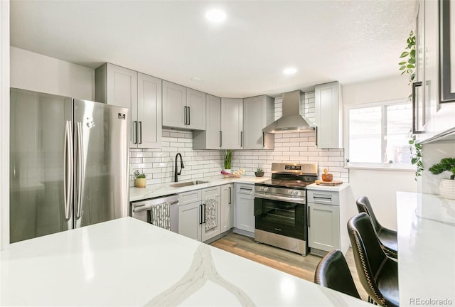 kitchen with stainless steel appliances, gray cabinets, wall chimney exhaust hood, and a sink