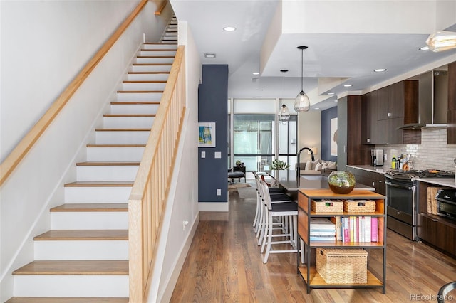 kitchen featuring dark brown cabinets, a kitchen breakfast bar, stainless steel range with gas stovetop, tasteful backsplash, and wall chimney exhaust hood