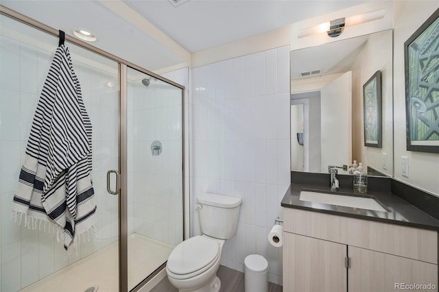 bathroom with vanity, a shower with door, tile walls, and toilet