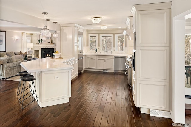 kitchen with a fireplace, white cabinetry, a breakfast bar area, hanging light fixtures, and dark wood-type flooring