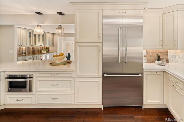 kitchen with dark hardwood / wood-style flooring, pendant lighting, stainless steel appliances, decorative backsplash, and cream cabinetry