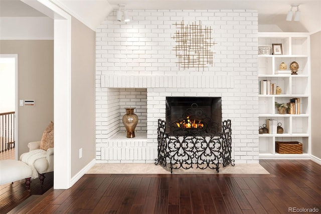 living room featuring lofted ceiling, ornamental molding, a brick fireplace, dark wood-type flooring, and built in shelves