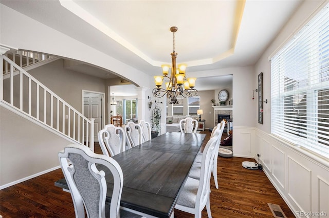 20366 Spruce Point Pl, Parker, CO 80134 - dining area featuring arched walkways, stairs, a chandelier, a tray ceiling, and ornate columns