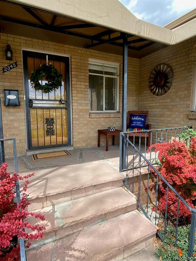 view of exterior entry with brick siding and a porch