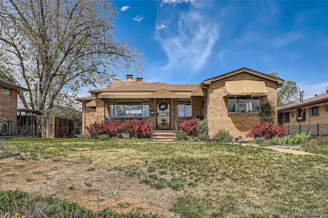 view of front of home featuring brick siding, fence, a chimney, and a front yard