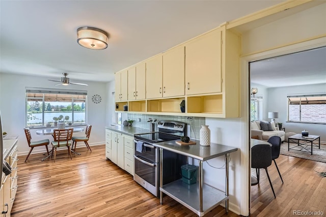 kitchen featuring light wood-style floors, a ceiling fan, backsplash, and double oven range