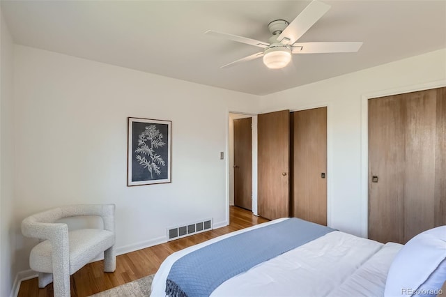 bedroom with ceiling fan, multiple closets, baseboards, wood finished floors, and visible vents
