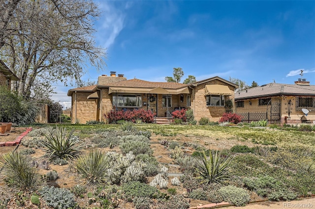 ranch-style house featuring fence, covered porch, a chimney, and brick siding