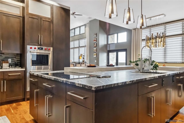 kitchen with oven, light wood-type flooring, a center island with sink, a sink, and tasteful backsplash