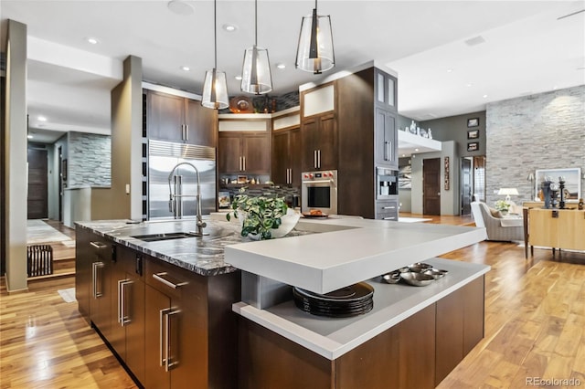 kitchen with light wood-type flooring, a large island, a sink, open shelves, and stainless steel appliances