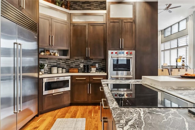 kitchen featuring open shelves, glass insert cabinets, appliances with stainless steel finishes, light wood finished floors, and decorative backsplash