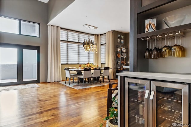 bar featuring beverage cooler, an inviting chandelier, and wood finished floors