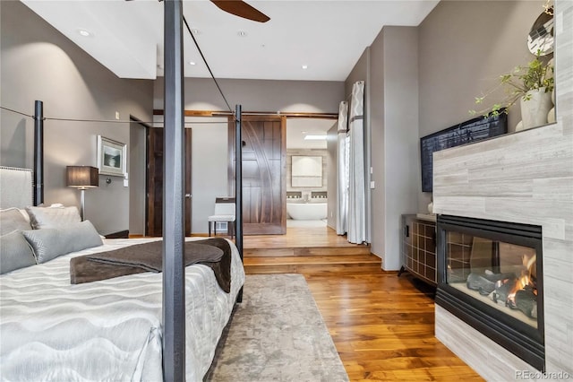 bedroom featuring wood finished floors, a fireplace, recessed lighting, a barn door, and connected bathroom