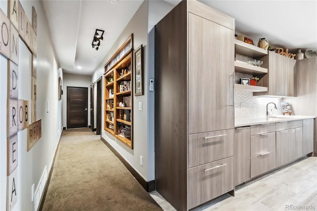 hall featuring a sink, visible vents, baseboards, and light colored carpet