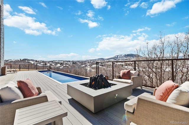 wooden deck featuring a fenced in pool, an outdoor living space with a fire pit, and a mountain view