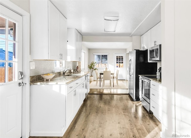 kitchen with white cabinetry, tasteful backsplash, light stone counters, appliances with stainless steel finishes, and hardwood / wood-style flooring