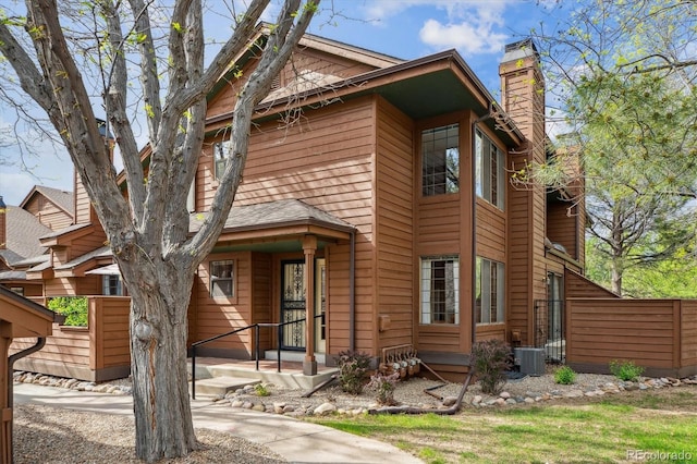 view of front facade featuring a chimney, central AC unit, and fence
