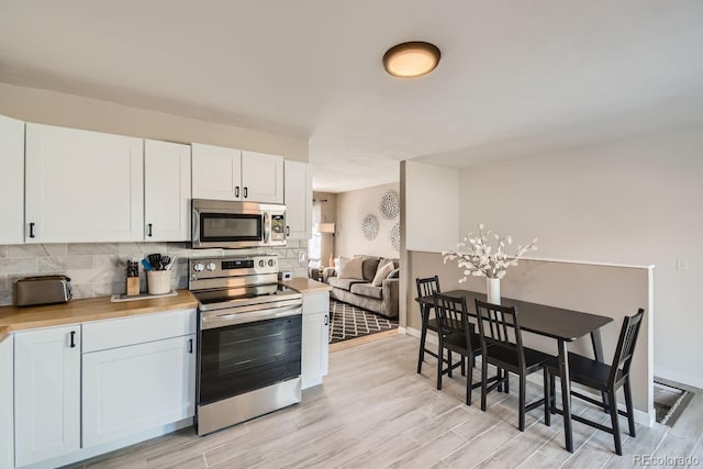 kitchen with light wood finished floors, light countertops, decorative backsplash, appliances with stainless steel finishes, and white cabinets