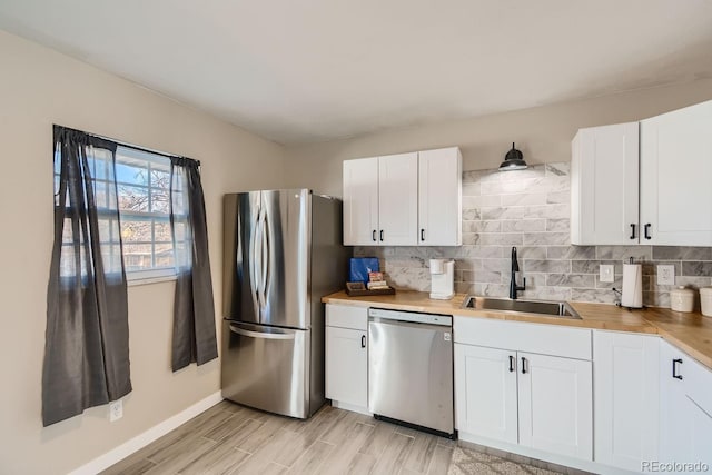 kitchen featuring tasteful backsplash, appliances with stainless steel finishes, white cabinetry, a sink, and light wood-type flooring