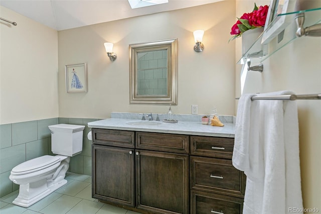 bathroom featuring a skylight, tile walls, vanity, toilet, and tile patterned floors