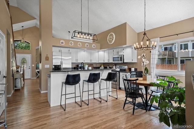 8051 W 78th Cir, Arvada, CO 80005 - kitchen featuring appliances with stainless steel finishes, high vaulted ceiling, dark countertops, a chandelier, and light wood-type flooring