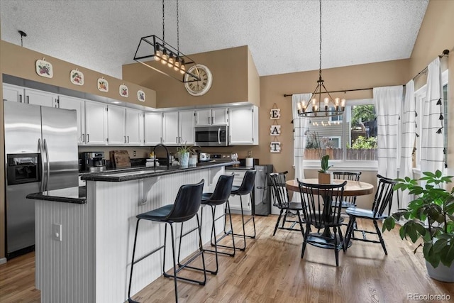 8051 W 78th Cir, Arvada, CO 80005 - kitchen with stainless steel appliances, lofted ceiling, a chandelier, dark countertops, and a textured ceiling