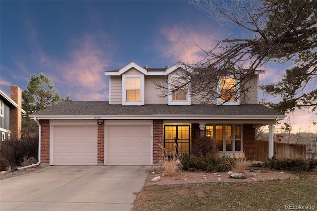 traditional-style home with fence, roof with shingles, concrete driveway, a garage, and brick siding