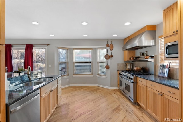 kitchen featuring recessed lighting, a sink, light wood-style floors, appliances with stainless steel finishes, and wall chimney exhaust hood