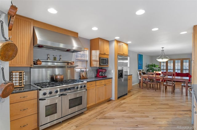 kitchen featuring dark countertops, light wood finished floors, appliances with stainless steel finishes, and wall chimney exhaust hood