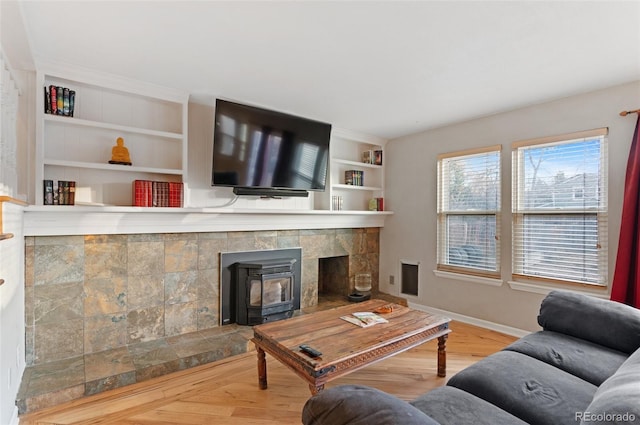 living area featuring baseboards, built in shelves, wood finished floors, and a wood stove