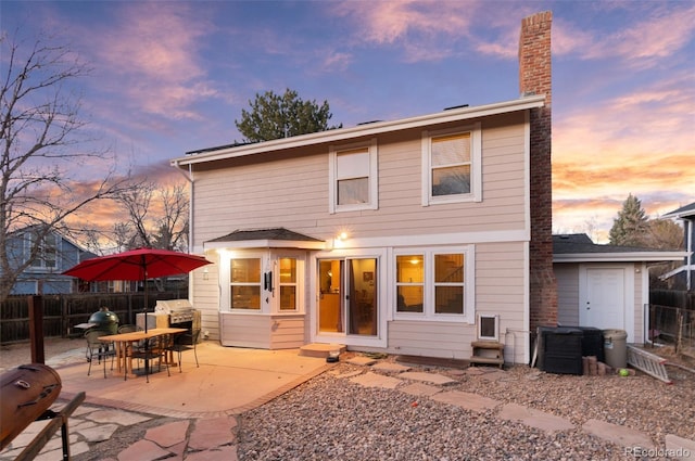 back of house at dusk with a patio, a chimney, and fence