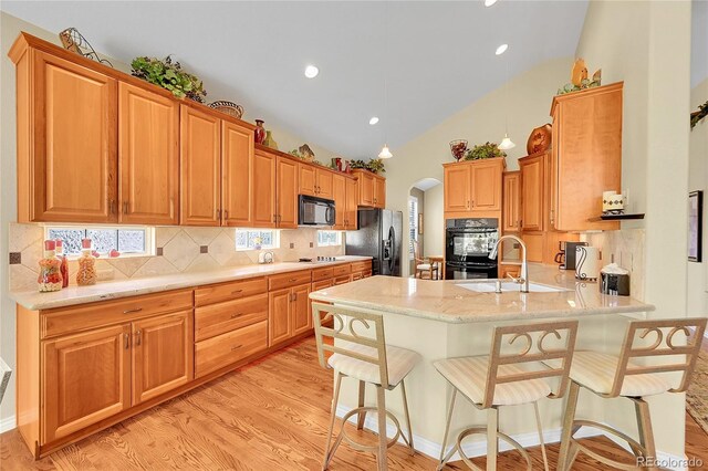 6696 S Quail Ct, Littleton, CO 80127 - kitchen with black appliances, arched walkways, a peninsula, light wood-type flooring, and decorative backsplash