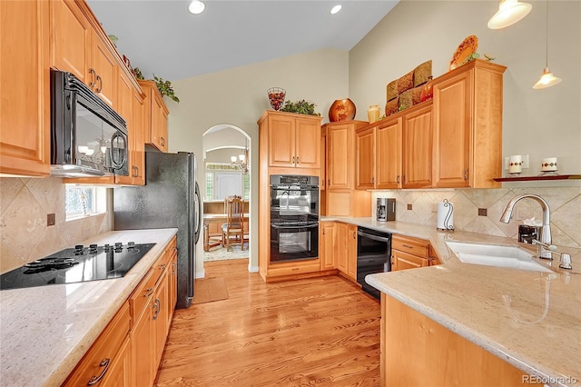 6696 S Quail Ct, Littleton, CO 80127 - kitchen with black appliances, arched walkways, light wood-style floors, light stone counters, and decorative light fixtures